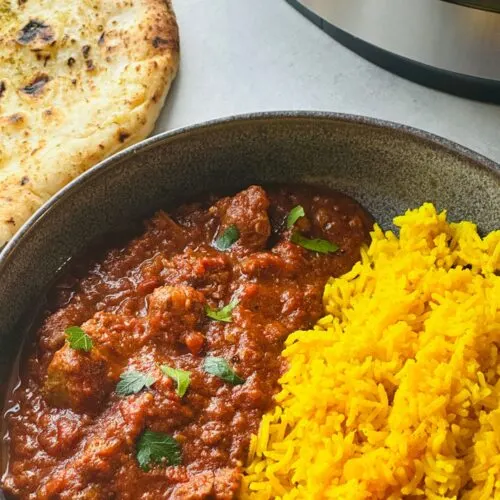 lamb madras curry next to pilau rice in a grey bowl next to a naan bread with part of the ninja foodi 15 in 1 behind it