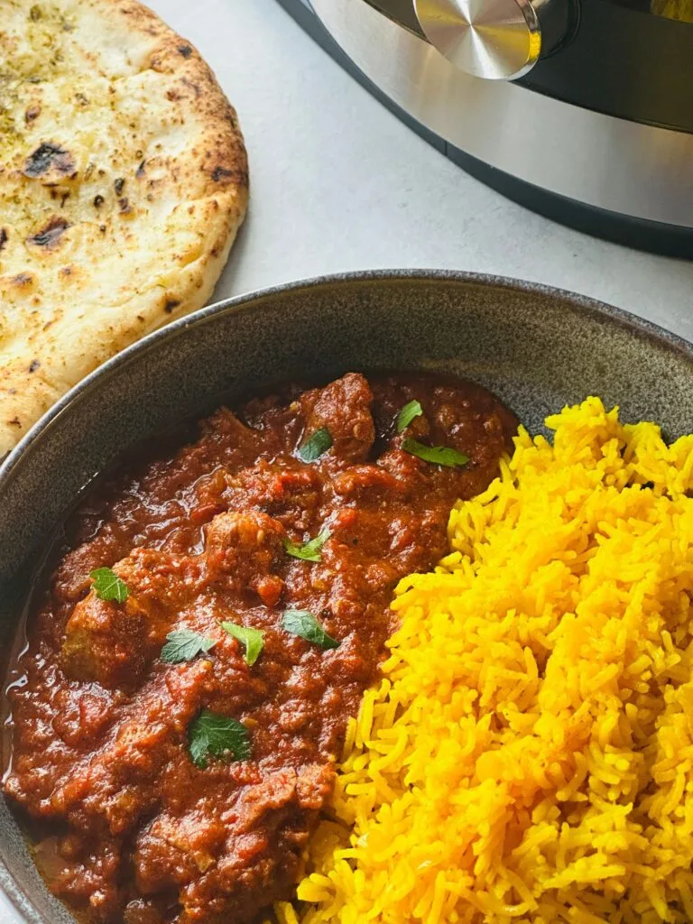 lamb madras curry next to pilau rice in a grey bowl next to a naan bread with part of the ninja foodi 15 in 1 behind it