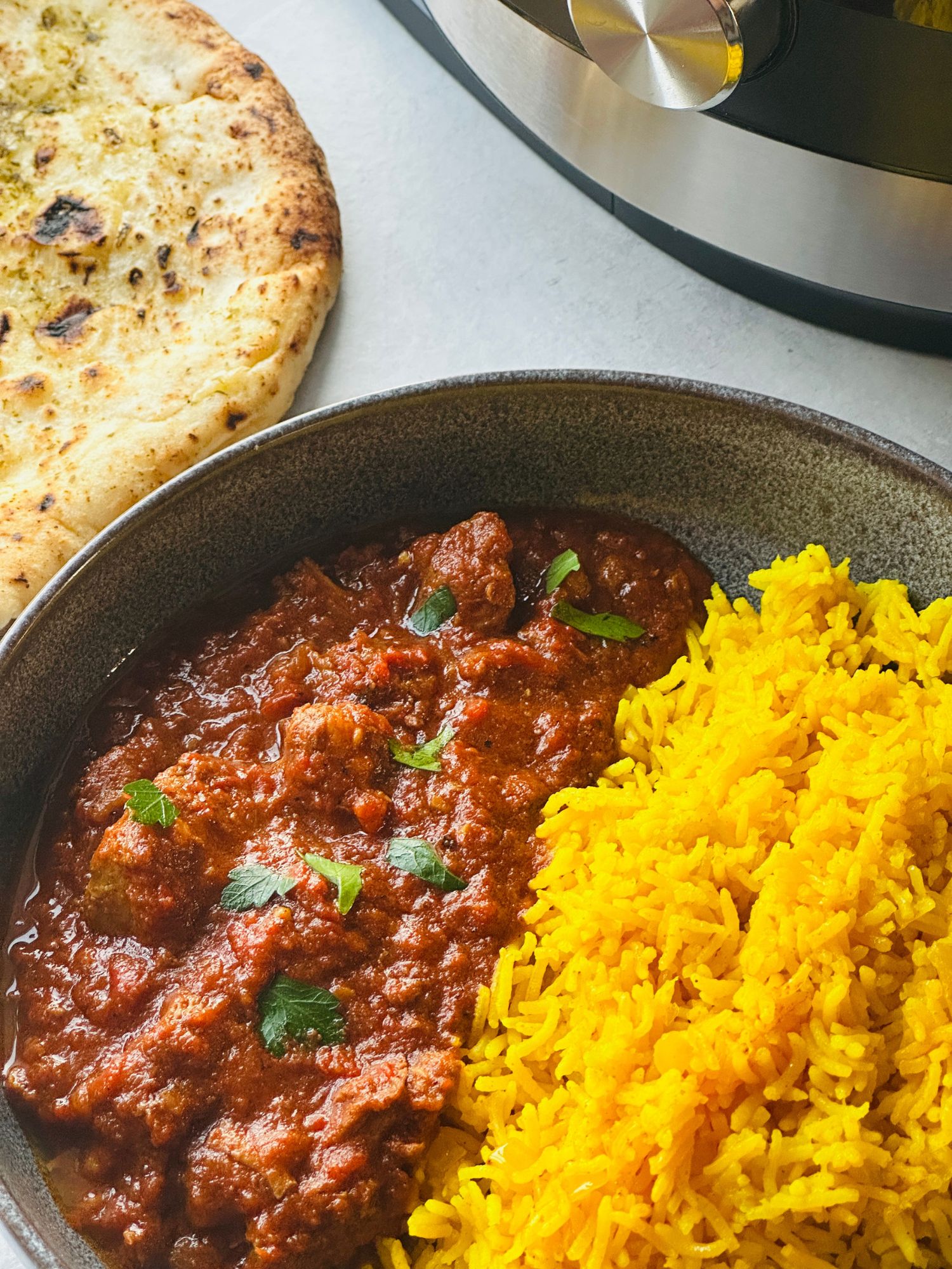 lamb madras curry next to pilau rice in a grey bowl next to a naan bread with part of the ninja foodi 15 in 1 behind it