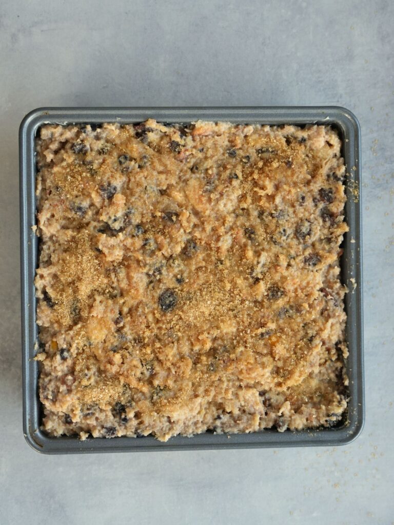 putting bread pudding mixture in tin  with demerara sugar on top