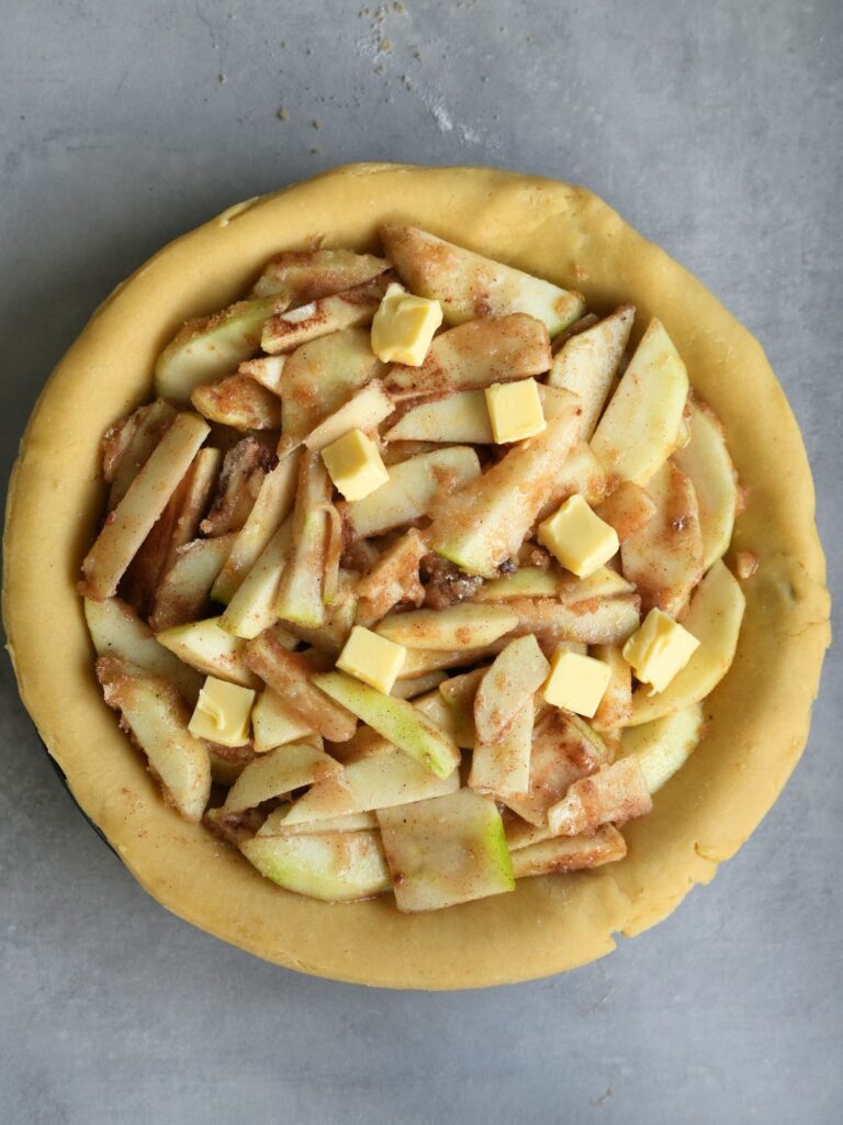 sliced apple with sugar and butter dotted on top in a pastry case
