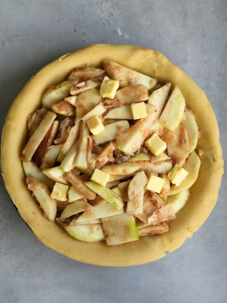 sliced apple with sugar and butter dotted on top in a pastry case