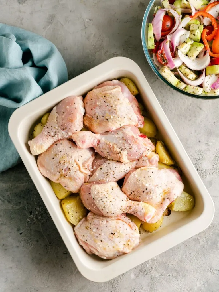 seasoned chicken thighs on potatoes ready to be roasted