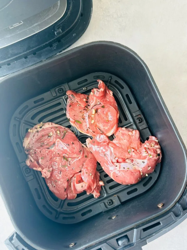 raw lamb steaks covered in olive oil, fresh garlic and fresh chopped rosemary in an air fryer basket