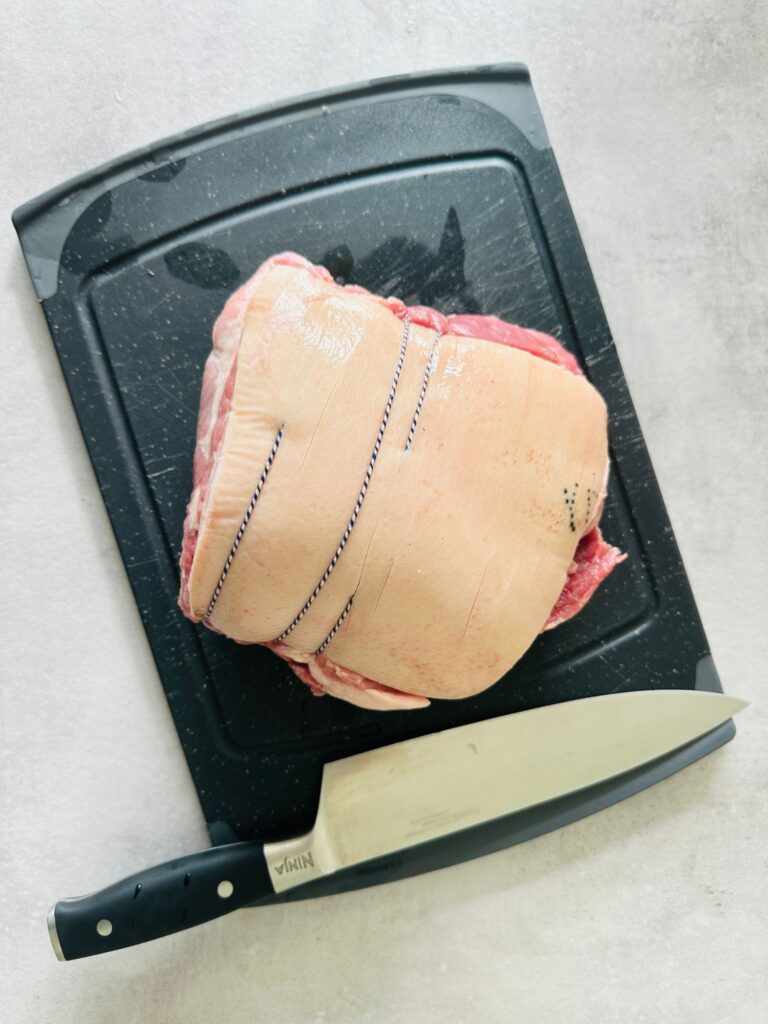 raw pork shoulder joint on a chopping board with a Ninja knife next to it.