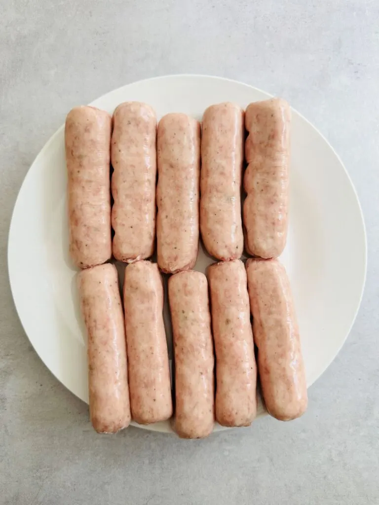 ten raw sausages laid out on a white plate