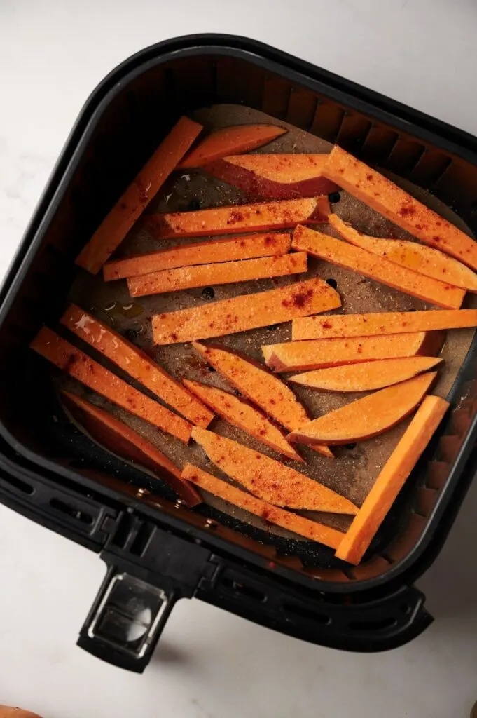 raw sweet potato fries in air fryer basket with seasoning