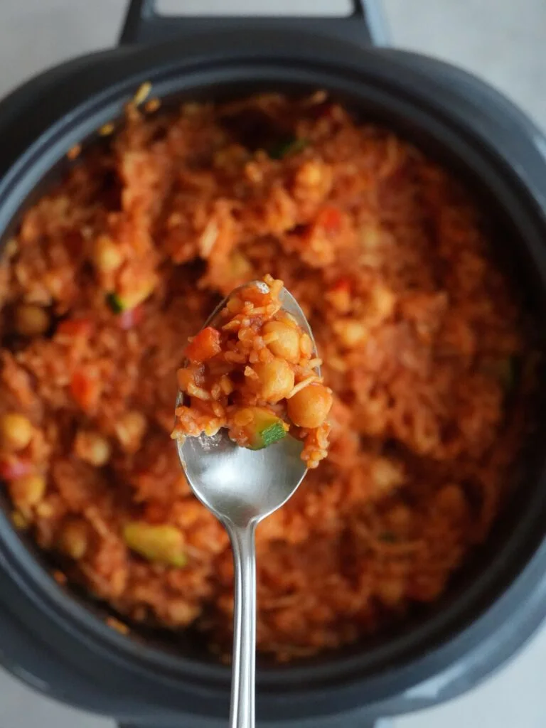 rice cooker with cooked meal of rice, chickpeas, red lentils, passata, vegetables with a spoonful above it