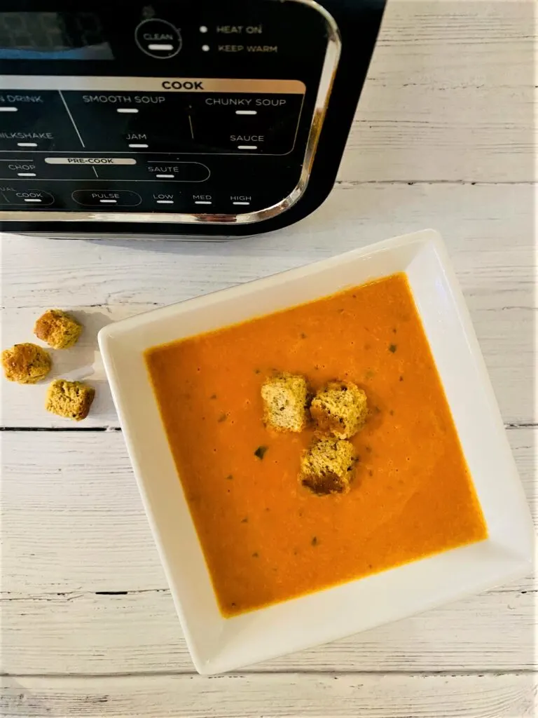 roasted red pepper tomato and mascarpone soup in a bowl with croutons next to Ninja Soup Maker