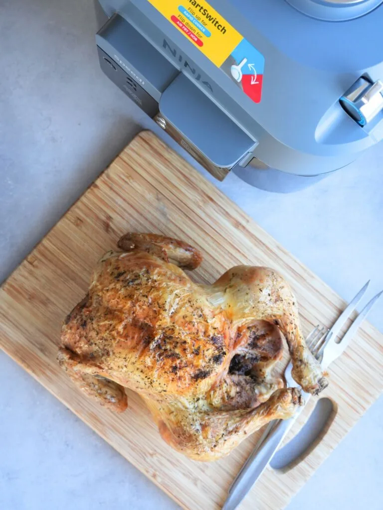 whole roasted chicken on a chopping board next to a Ninja Speedi