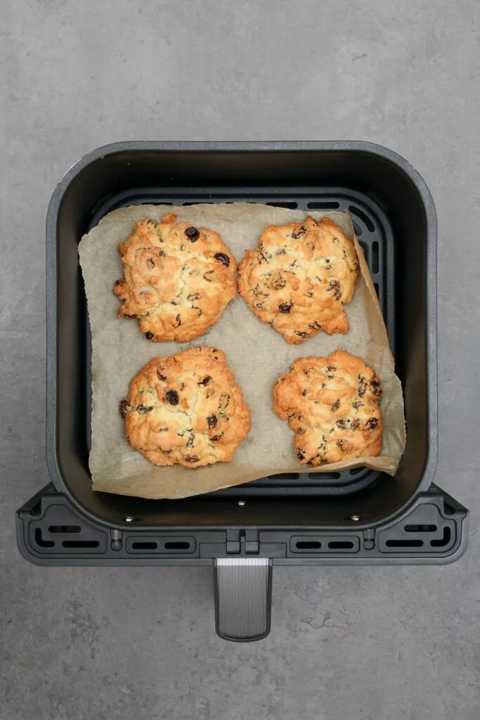 four cooked rock cakes in air fryer basket on baking paper