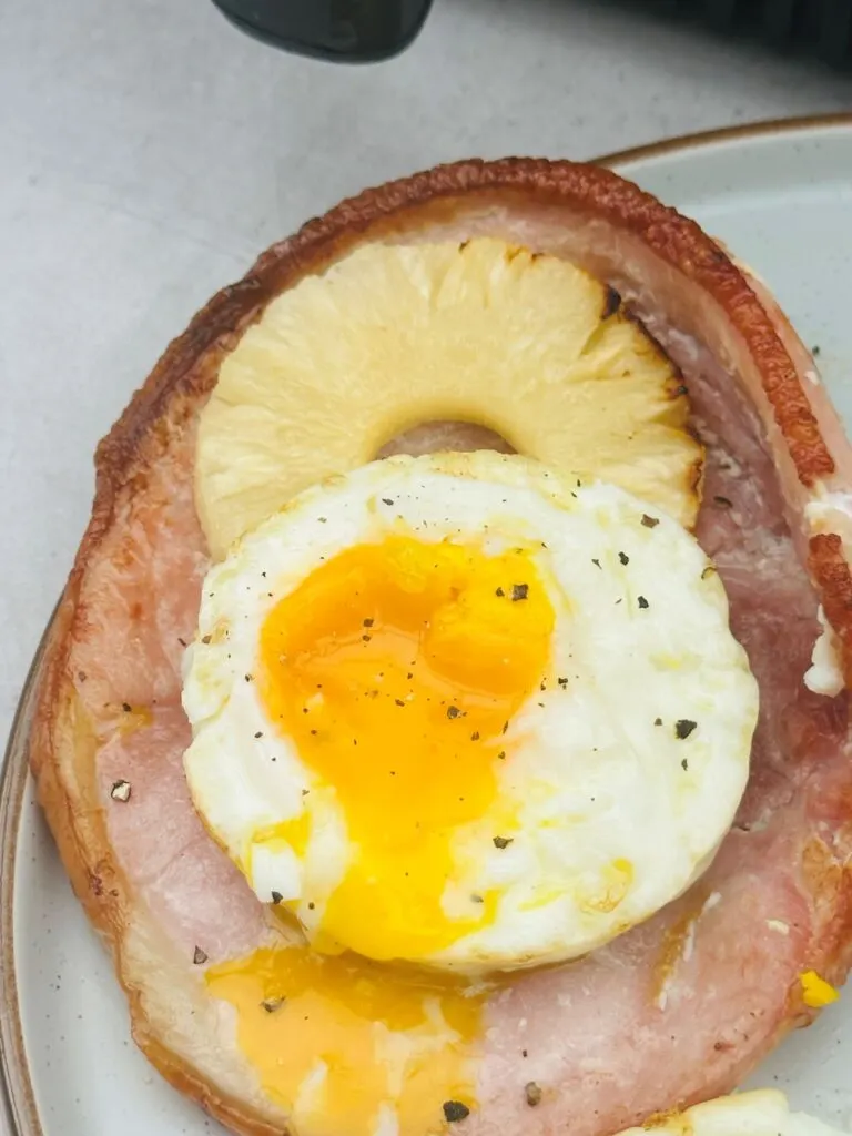 runny fried egg on top of cooked gammon steak and a pineapple ring