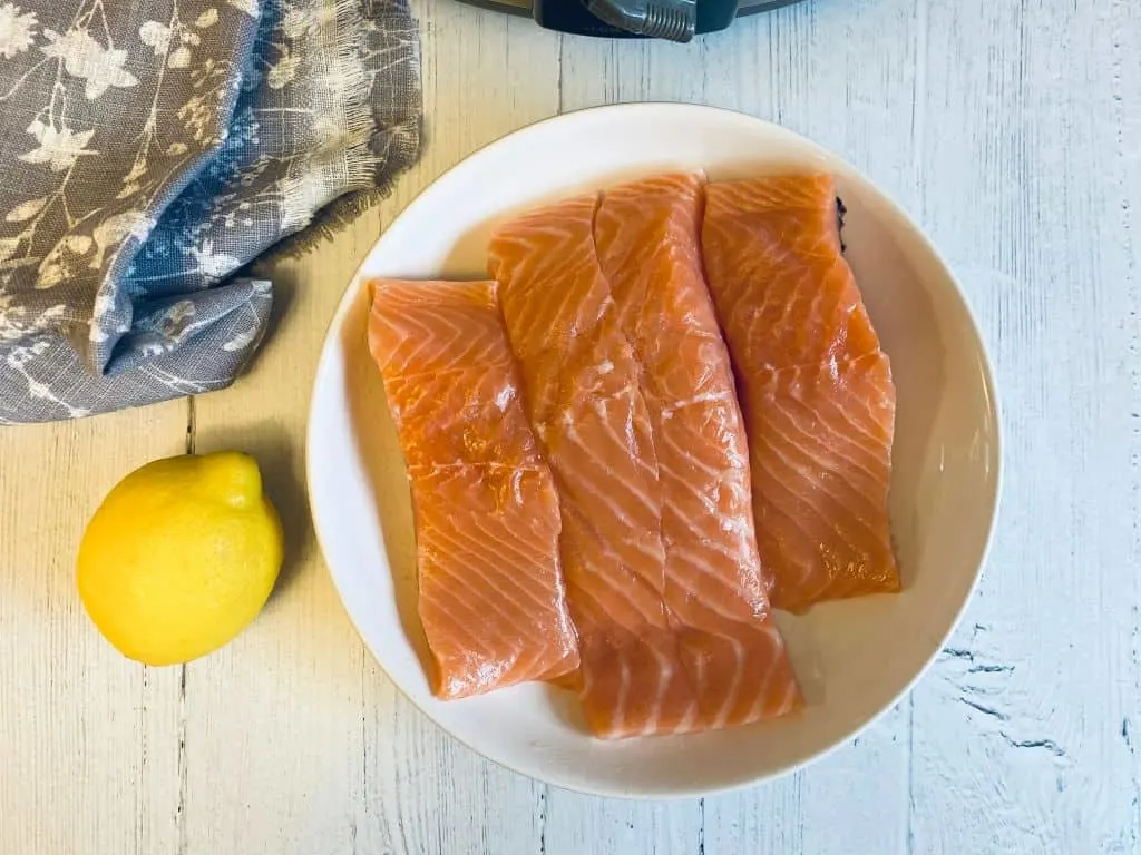 4 slices of raw salmon next to a lemon and slow cooker