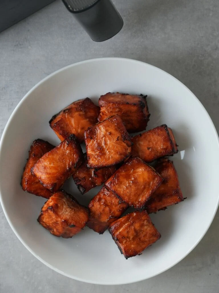 cooked salmon bites in a white bowl next to an air fryer