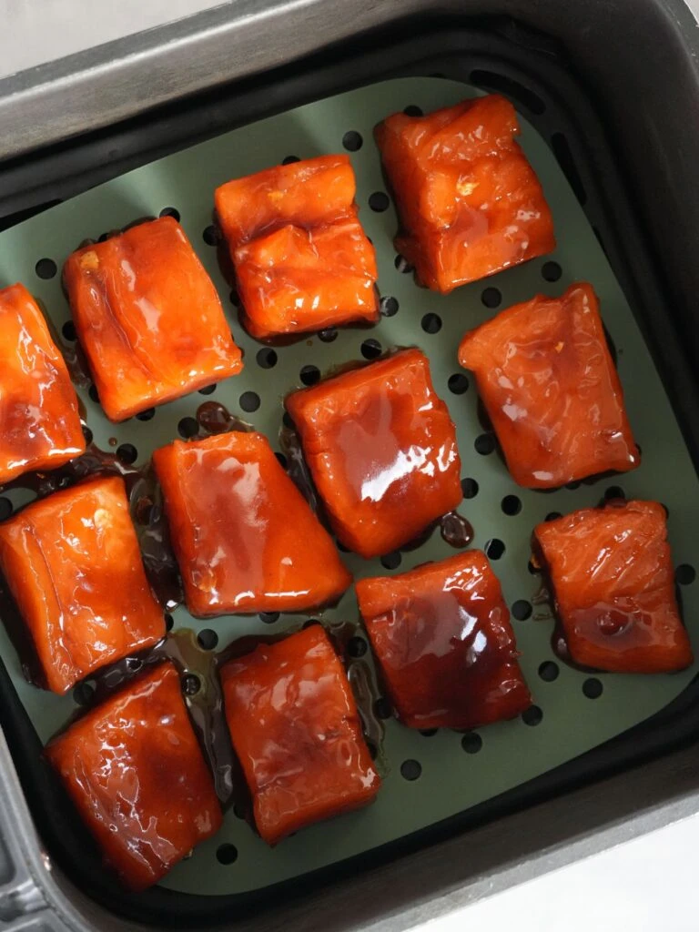 salmon cut into bites covered in sauce and in air fryer basket ready