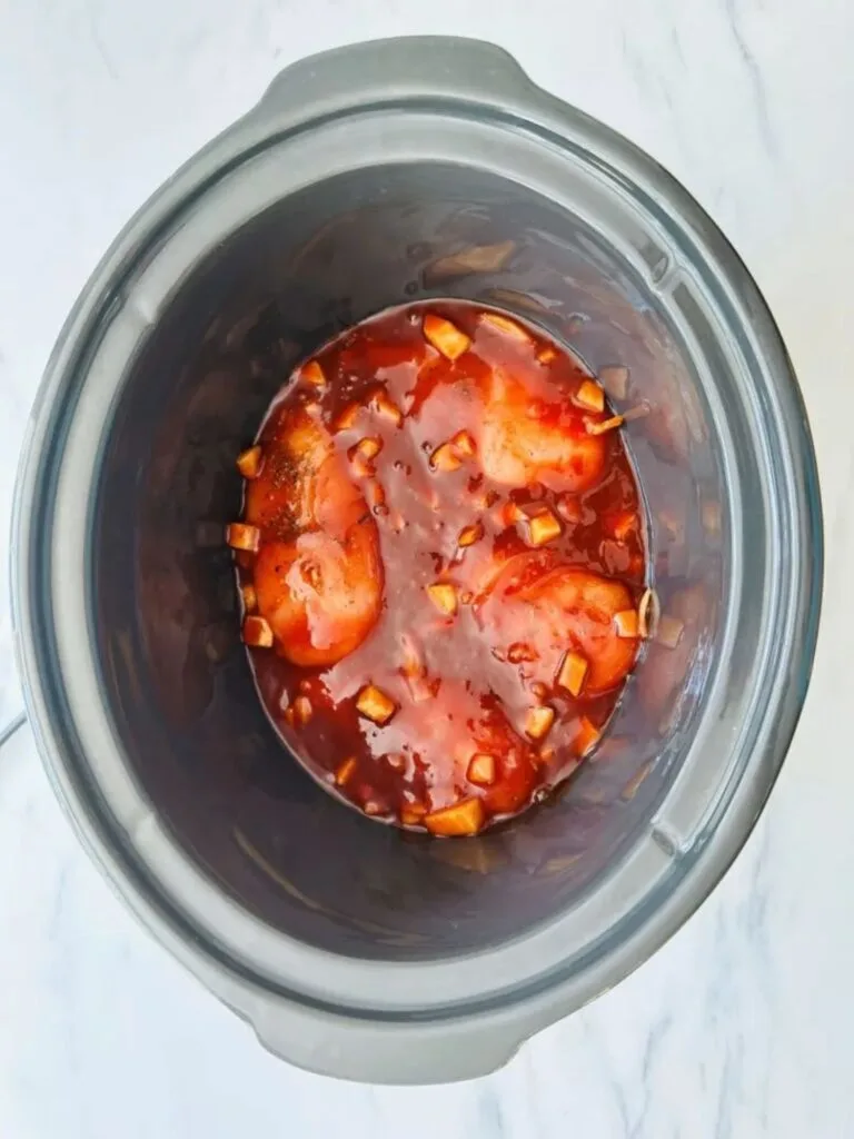 sauce poured over raw chicken in a slow cooker
