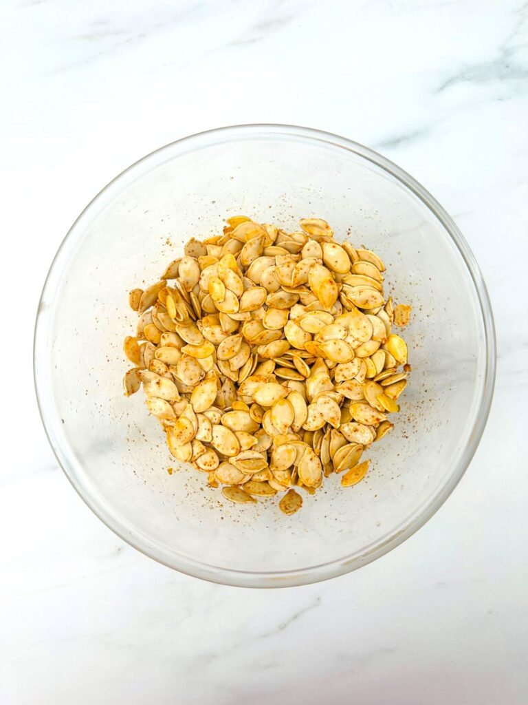 seasoning pumkin seeds in a glass bowl