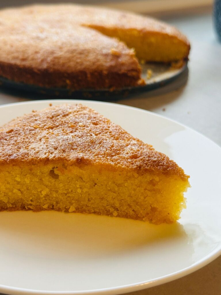slice of lemon polenta cake on a plate in front of the remaining cake