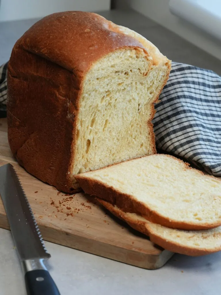 loaf of Brioche sliced on a wooden chopping board with a bread knife next to it