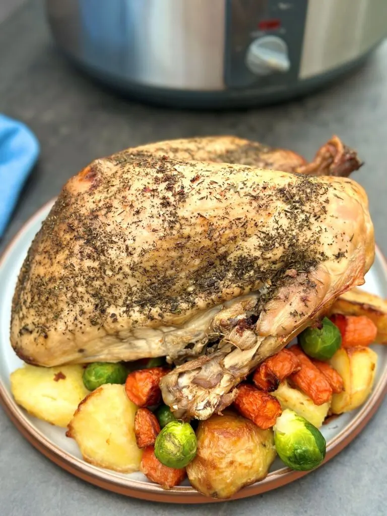 slow cooked turkey crown on a plate of roasted vegetables next to a slow cooker