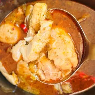 Thai red curry chicken in a large serving spoon lifted up above a slow cooker