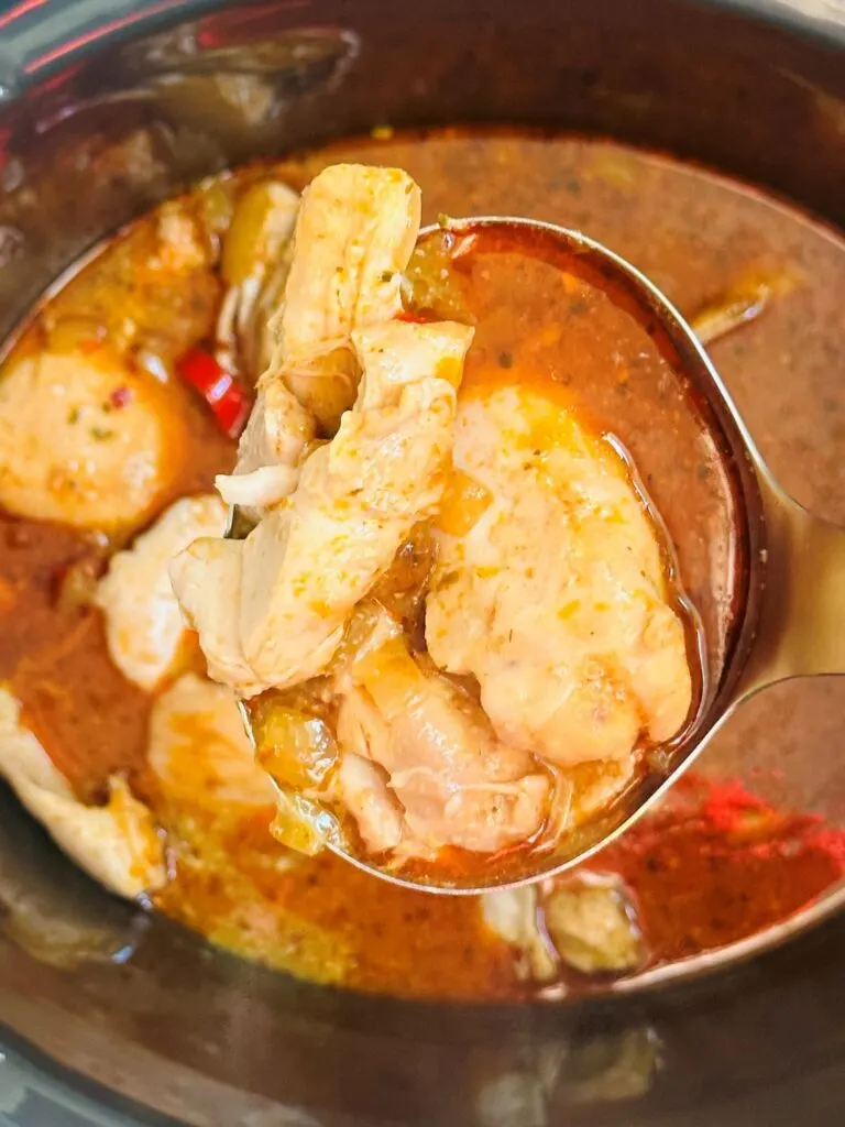 Thai red curry chicken in a large serving spoon lifted up above a slow cooker