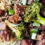 slow cooked beef and broccoli served with noodles and garnished with sesame seeds, chopped spring onions