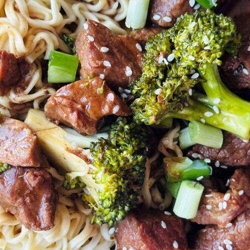 slow cooked beef and broccoli served with noodles and garnished with sesame seeds, chopped spring onions