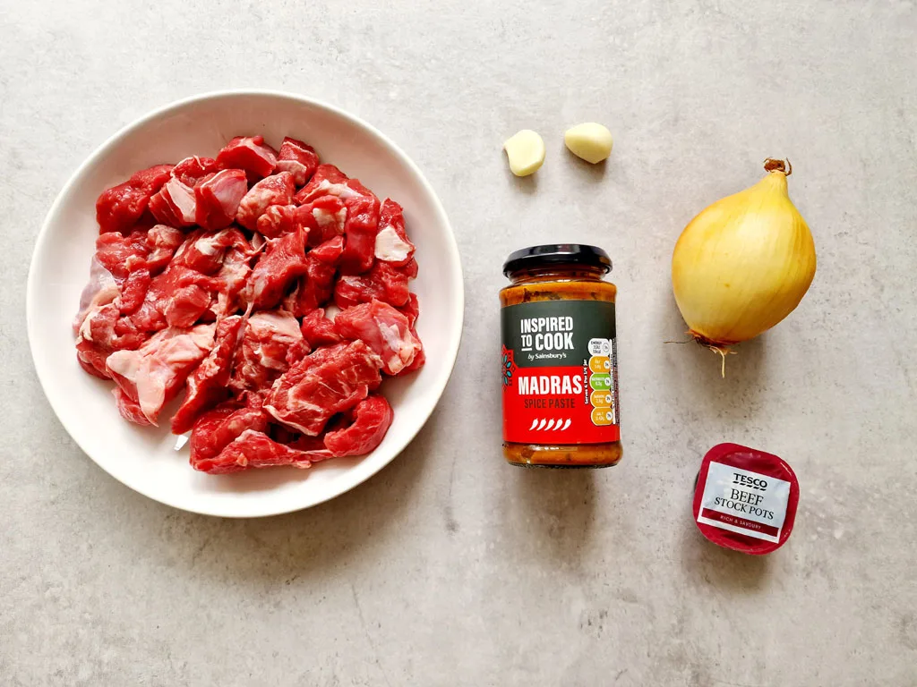 ingredients for making easy slow cooker beef madras, diced beef, madras spice paste, onion, 2 garlic cloves and 1 beef stock pot