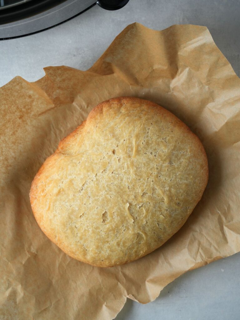 loaf of bread cooked in a slow cooker resting on some greaseproof paper