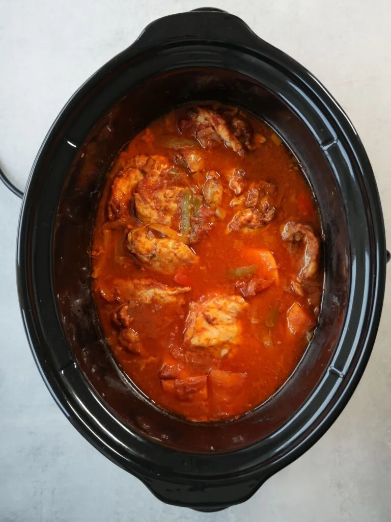 slow cooker with cooked chicken and sweet potato in a harissa flavoured tomato sauce