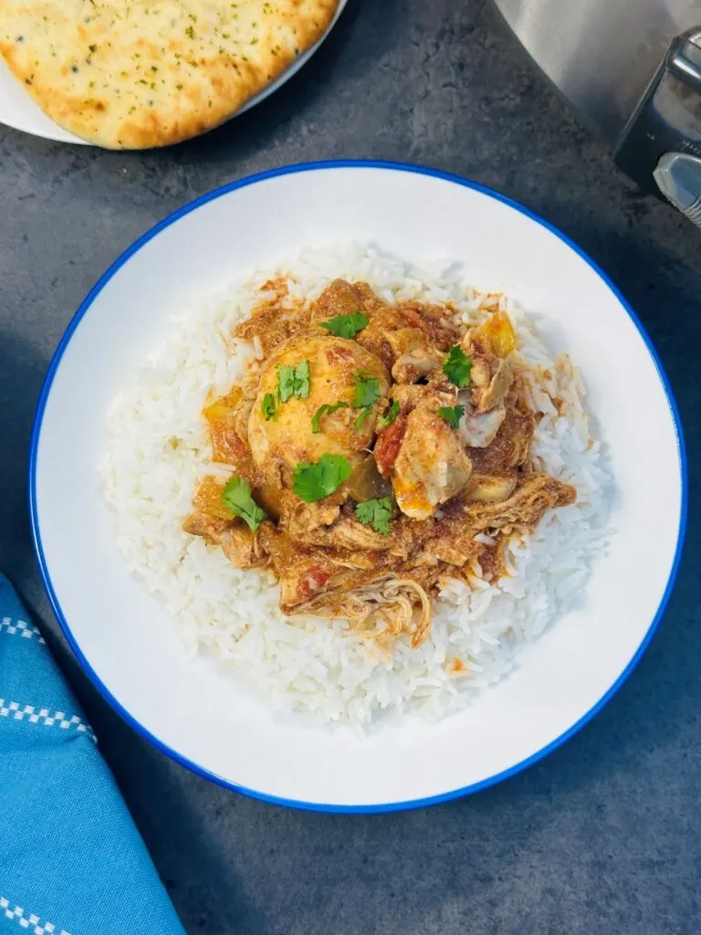 chicken curry on a plate with rice next to a nan bread and slow cooker