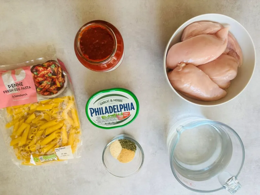 ingredients for slow cooker chicken pasta: chicken breasts, water, pasta sauce, Philadelphia garlic and herb cream cheese, penne pasta and dried herbs