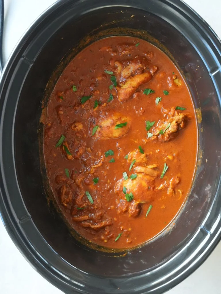 cooked chicken tikka masala in a slow cooker with fresh chopped coriander garnished on top