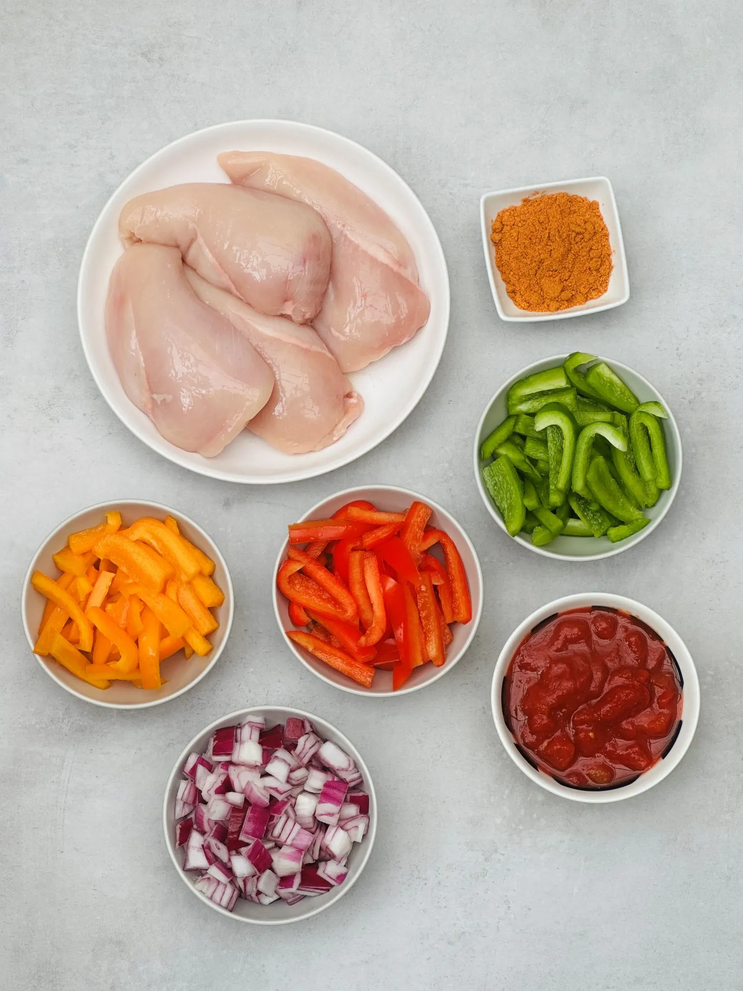 ingredients for slow cooker chicken fajitas: 4 chicken breasts, fajita spice mix, chopped orange, red and green peppers, chopped red onions and chopped tomatoes