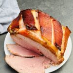 slow cooked gammon in coke, sliced on a white plate with grey tea towel