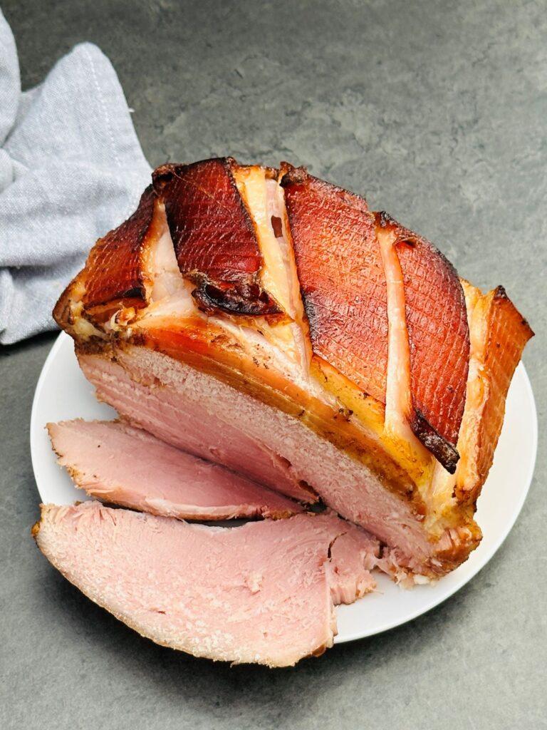 slow cooked gammon in coke, sliced on a white plate with grey tea towel 