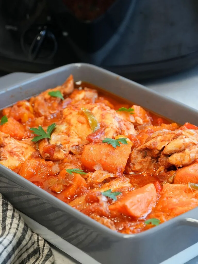 chicken and sweet potato cooked in a harissa paste in a grey and white dish in front of a slow cooker
