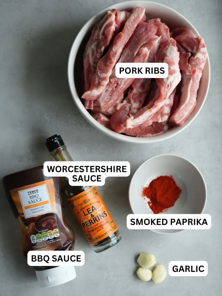 ingredients laid out and labelled for slow cooker pork ribs: pork ribs, Worcestershire sauce, smoked paprika, BBQ sauce and garlic cloves