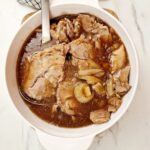 pork shoulder cooked and sliced in a serving bowl with a serving spoon in it