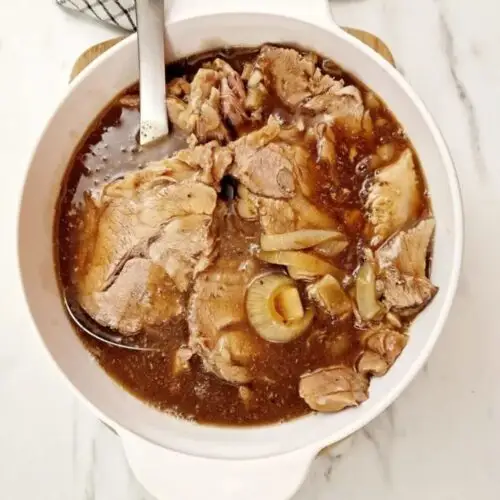 pork shoulder cooked and sliced in a serving bowl with a serving spoon in it