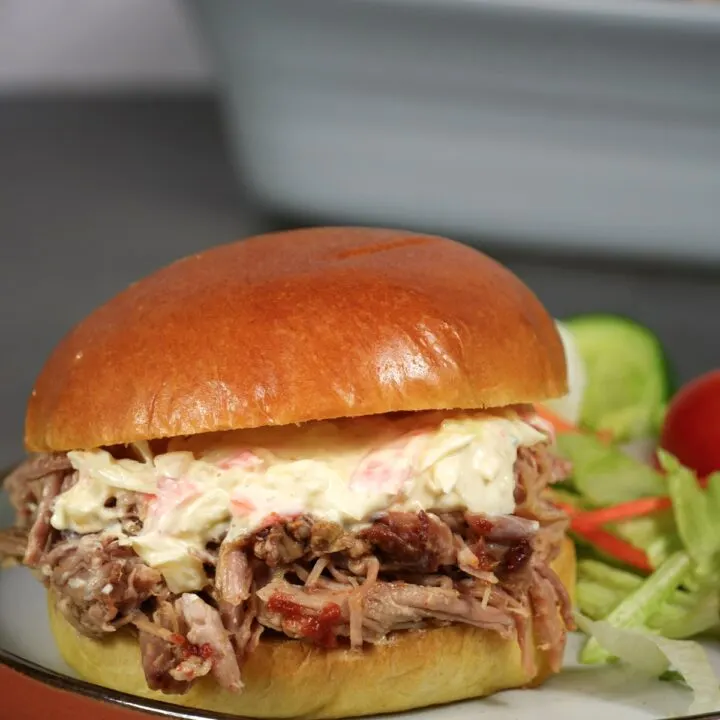 slow cooker pulled pork in a brioche bun with salad on the plate