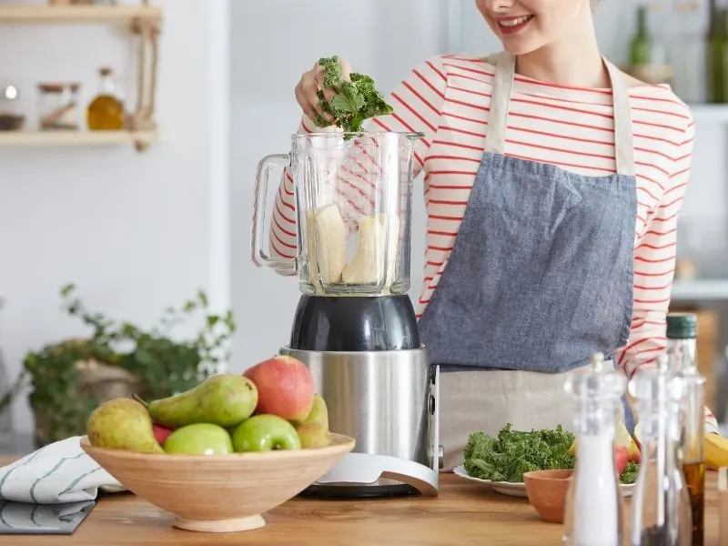 making a smoothie in a blender with fruit bowl next to it