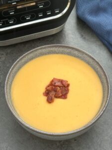 lentil and bacon soup in a grey bowl with crispy bacon on top next to a Ninja soup maker
