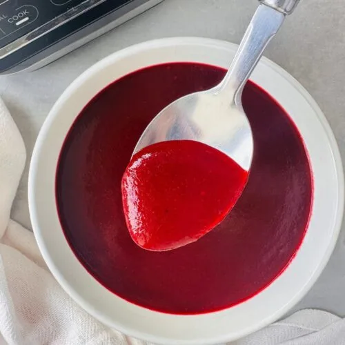 beetroot soup in a white bowl with a spoon held above it next to a white cloth and part of the ninja soup maker base in the corner