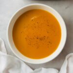 carrot and swede soup in a white bowl next to a ninja soup maker