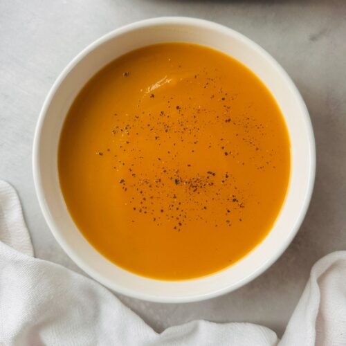 carrot and swede soup in a white bowl next to a ninja soup maker