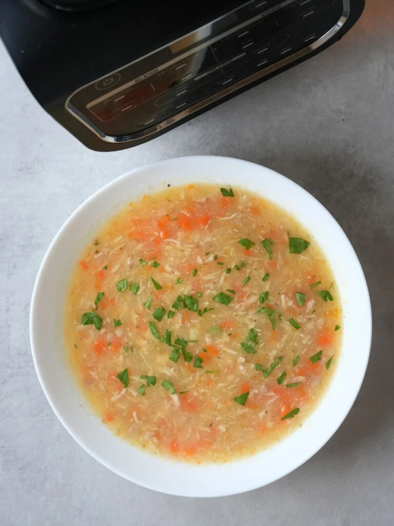 chicken and potato soup in a bowl with carrots and fresh parsley. part of the base of the ninja soup maker can be seen in the corner of the picture