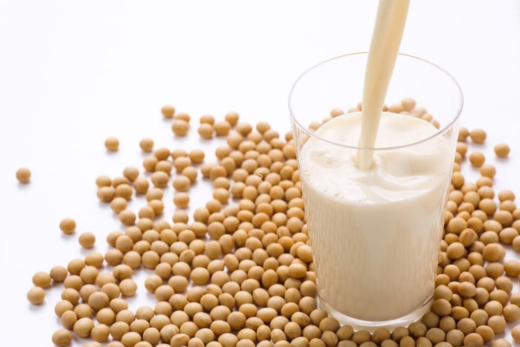 soy milk being poured into glass with soy beans next to it