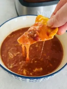 tortilla chip dipped into a spicy bean soup with melted cheese next to a Ninja soup maker